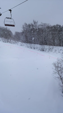 Winter scene at Shiga Kogen Nishitateyama Ski Area in Japan featuring a skier navigating snow-covered slopes near a chalet, set against a pristine winter backdrop.