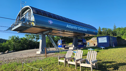 Image of a sunny day at Ski Cape Smokey in Nova Scotia, Canada, featuring a scenic ski lift ascending towards a cozy chalet nestled in the snowy mountain resort.