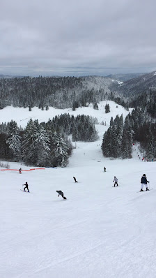 Skiers enjoying a day at La Bresse-Hohneck ski resort in La Bresse, France, amid a winter landscape. A challet can be seen in the backdrop.