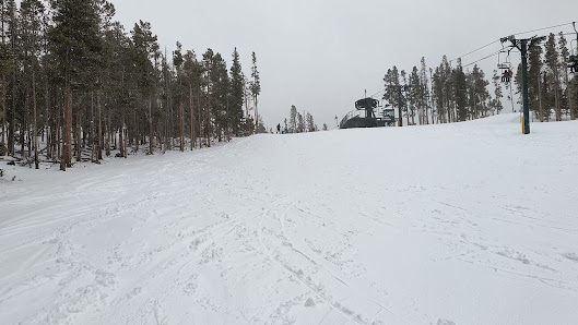 A winter sports scene at Snowy Range in Centennial Wyoming showcasing a ski resort with a ski lift. Skiers and a snowmobile can be spotted enjoying the wintry landscape.