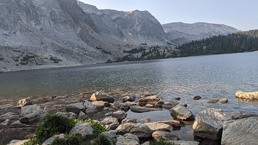 A scenic view of Snowy Range in Centennial Wyoming showcasing a serene lake nestled by a vast mountain range under the clear blue sky.