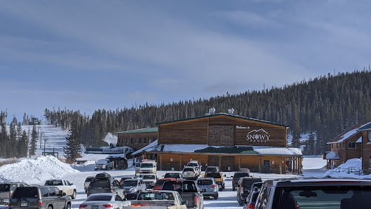 Ski resort at Snowy Range in Centennial, Wyoming featuring wide, snow-covered slopes. The surrounding scene depicts a lively winter sports atmosphere with a distant view of a lodge and a ski lift.