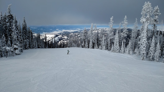 A skier gliding down the pristine snow-covered slopes of Blacktail Mountain in Lakeside, Montana. Surroundings feature a buzzy winter sports scene with the ski lift of the resort visible.