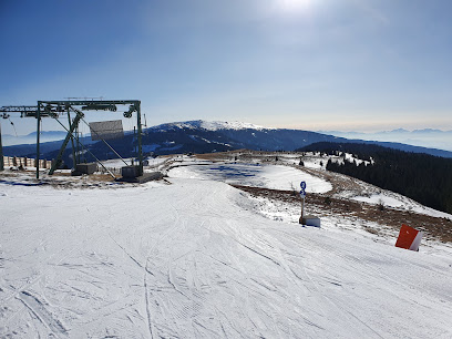 A winter scene at Klippitztörl ski resort in Austria featuring a ski lift transporting people uphill while a skier glides down the snow-covered slope. Snowy chalets are also present in the background.
