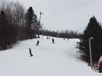 Winter sports scene at Labrador Mountain in Truxton, NY, featuring skiers enjoying the snowy slopes, ascending via ski lift to the top of the ski resort.