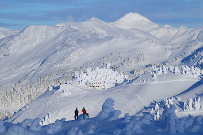 Ski resort scene at Eaglecrest in Juneau, Alaska with people engaged in winter sports. The winter setting includes a chalet nestled amidst snowy mountains.