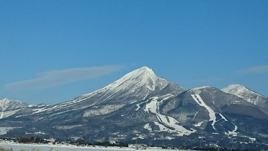 Stunning winter landscape in Grand Sunpia Inawashiro Snow Paradise, featuring a majestic mountain covered in snow with a charming chalet nestled at its base.