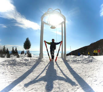 A winter scene at Grand Sunpia Inawashiro Snow Paradise showcasing a skier and a snowboarder in action. A ski lift can be seen in the background, amidst the snow-covered setting.