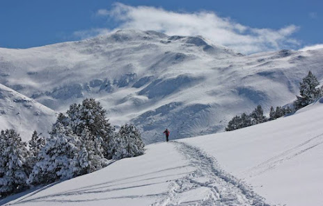 A chalet stands amidst a bustling winter sports scene at the Puigmal ski resort in Pyrénées-Orientales France with a skier making their way downhill amidst the snowy landscape.