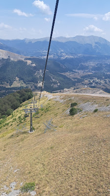 A ski lift against a snowy backdrop in Pescasseroli Italy. A challet is also visible in the distance. A skier readies to descend and a mountain can be faintly seen. The setting is truly a picturesque ski resort.