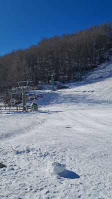 A ski lift and a chalet sit amidst a winter sports scene at the ski resort in Pescasseroli, Abruzzo, Italy. A skier is visible in the distance, enjoying the snowy slopes.