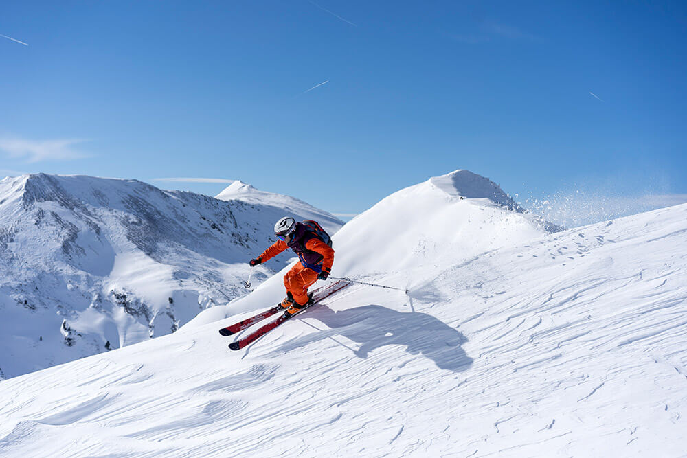 A skier enjoying a winter sports scene at Planneralm in Schladming-Dachstein, Austria. The setting includes a distant chalet amidst a bustling ski resort.