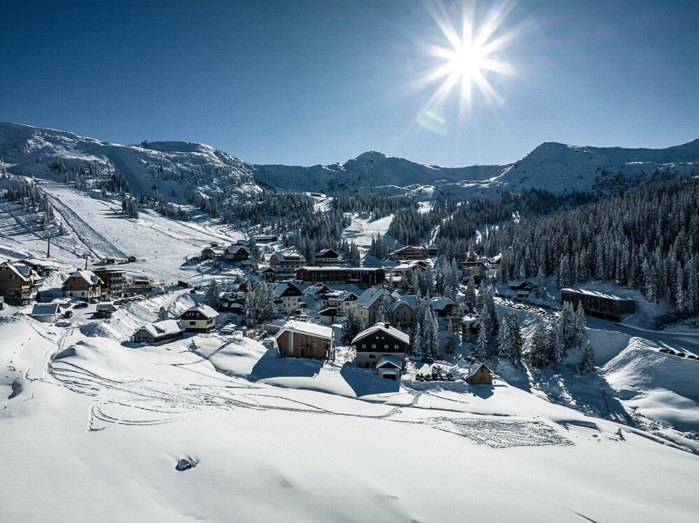 A winter scene at Planneralm ski resort in Austria featuring skiers enjoying winter sports amidst snowy mountains and a cozy chalet visible in the background.