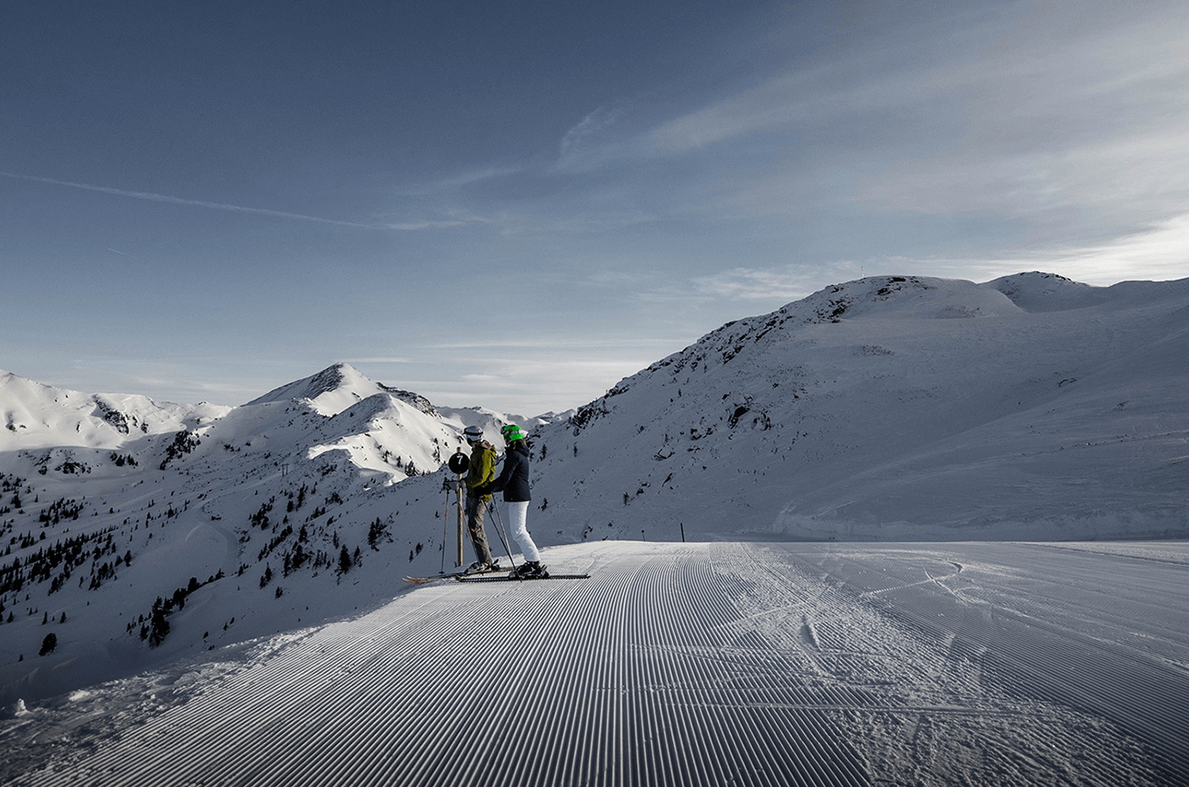A skier enjoying their time at the Planneralm in Schladming-Dachstein Austria with a chalet and robust winter sports center visible in the background of a bustling ski resort.