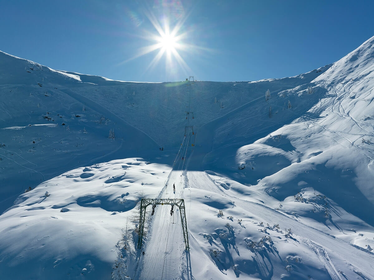 A winter scene at Planneralm in Austria displaying a bustling ski resort with a visible ski lift. Skiers enjoy the slopes amidst charming chalets in this serene snowy setting.