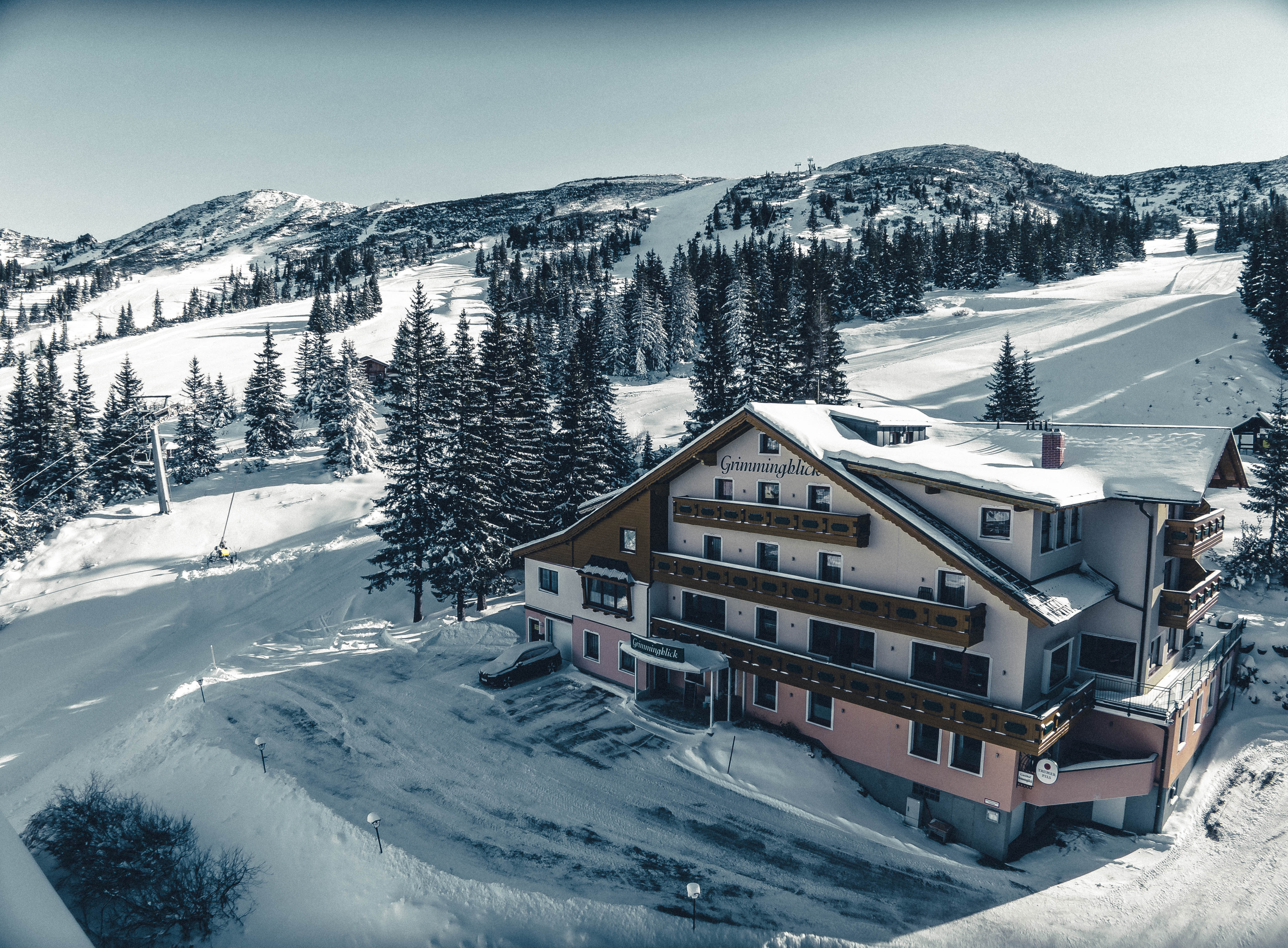 View of the Planneralm ski resort in Schladming-Dachstein, Austria featuring a charming mountain hut, a cosy chalet, and a bustling winter sports centre amidst snowy landscape.