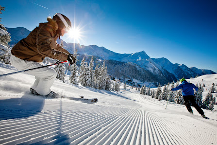 Winter scene at Planneralm, Schladming-Dachstein, featuring a skier in the foreground, a snowboarder in the distance, and several people enjoying skiing at the resort.