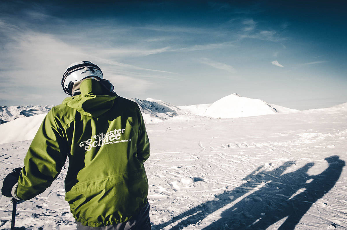A skier and a snowboarder enjoying a winter sports scene at Planneralm in Schladming-Dachstein, Austria. A quaint chalet and the sweeping landscape of the ski resort form a picturesque backdrop.