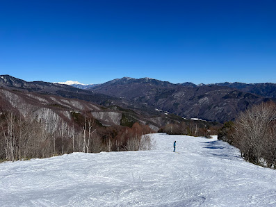 A picturesque view of Yabuhara Kogen Ski Resort in Nagano, Japan. The scene captures the vibrant atmosphere of winter sports, with a skier in motion, the ski lift operating, and the inviting chalet nestled in the snowy landscape.