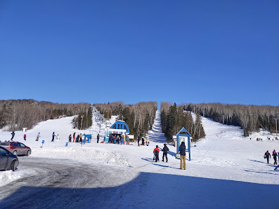 Winter scene at Mont Béchervaise, Gaspé, Quebec with a ski resort seen in the backdrop. Skiers utilize a ski lift to reach the peak, ready to enjoy the winter sports facilities available.