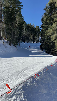 A skier navigating a snowy slope at Sipapu ski resort in Vadito New Mexico with a chalet in the backdrop and a group of skiers nearby.