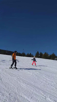 A family enjoying a day of skiing at Adria Ski–Kupres in Bosnia and Herzegovina, including a young child learning to ski. A picturesque chalet and winter sports scene add to the fun-filled ambiance.