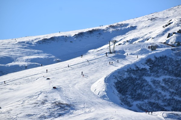 Winter sports enthusiasts enjoying a day at the Pian Munè ski resort in Piedmont, Italy, with snow-covered slopes and a charming chalet in the backdrop.