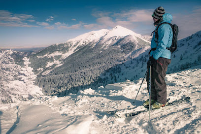A skier and a snowboarder enjoying winter sports at the Panarotta 2002 ski resort in Trentino, Italy, with a cozy challet in the backdrop, surrounded by the stunning Sugana Valley.