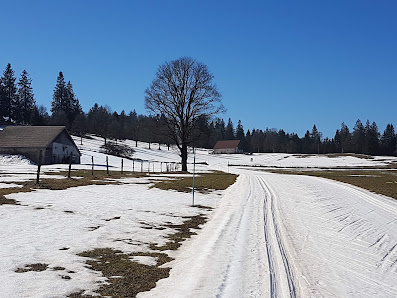 Scenic view of a chalet in Bugnenets-Savagnières, Switzerland amid a snowy landscape, providing a stunning backdrop to an active winter sports scene at a local centre.