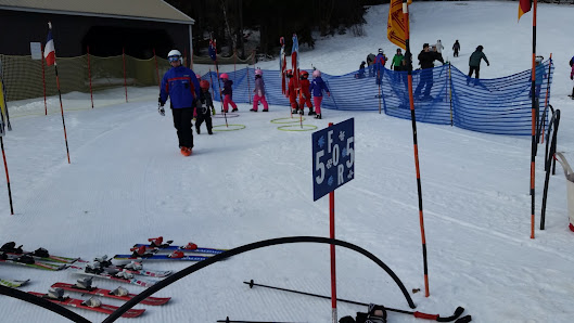 Vibrant winter sports scene at Middlebury Snowbowl in Vermont, with a skier cruising down a white-covered slope. The warm glow of a chalet and infrastructure of the resort under a clear sky are discernible in the background.