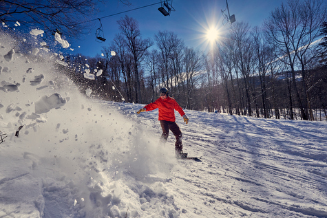 A skier and snowboarder enjoying a winter sports scene at the scenic Middlebury Snowbowl ski resort in Vermont, with a ski lift dotting the snowy landscape.