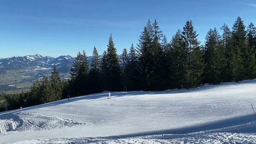 A winter sports scene at Bödele, Bregenz in Austria, featuring a skier gliding down the snow covered slopes of a ski resort with a charming chalet and scenic mountain backdrop.