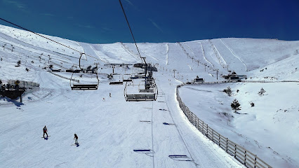 A scenic view of Valdesquí ski resort in Madrid Spain featuring a ski lift going up the snow-covered slopes with a challet in the backdrop buzzing with winter sports activities.