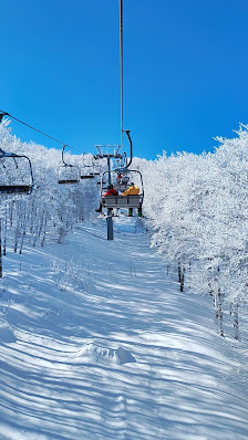 View of a ski lift in Monte Catria, Pesaro-Urbino with a scenic winter landscape in the background. The area is popular for winter sports with a few skiers visible in the distance.