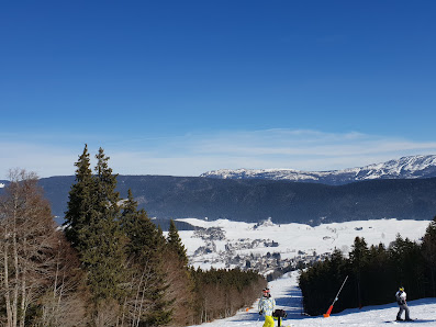 A chalet nestled in the striking winter landscape of Autrans-Méaudre in Isère, Grenoble. Scene encapsulates the quintessential ski resort ambiance, highlighted by the presence of a skier and a winter sports centre.