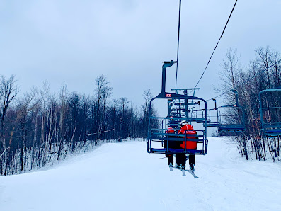 View from the top of Sommet Morin Heights in Quebec, Canada, featuring a ski lift adjacent to a snowy ski slope with a handful of skiers enjoying the wintry landscape.