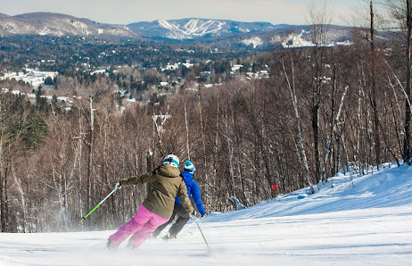 Winter sports scene at Sommet Morin Heights in Quebec, Canada, featuring a skier navigating the snowy slopes while others, including a family and a child learning to ski, enjoy the day.