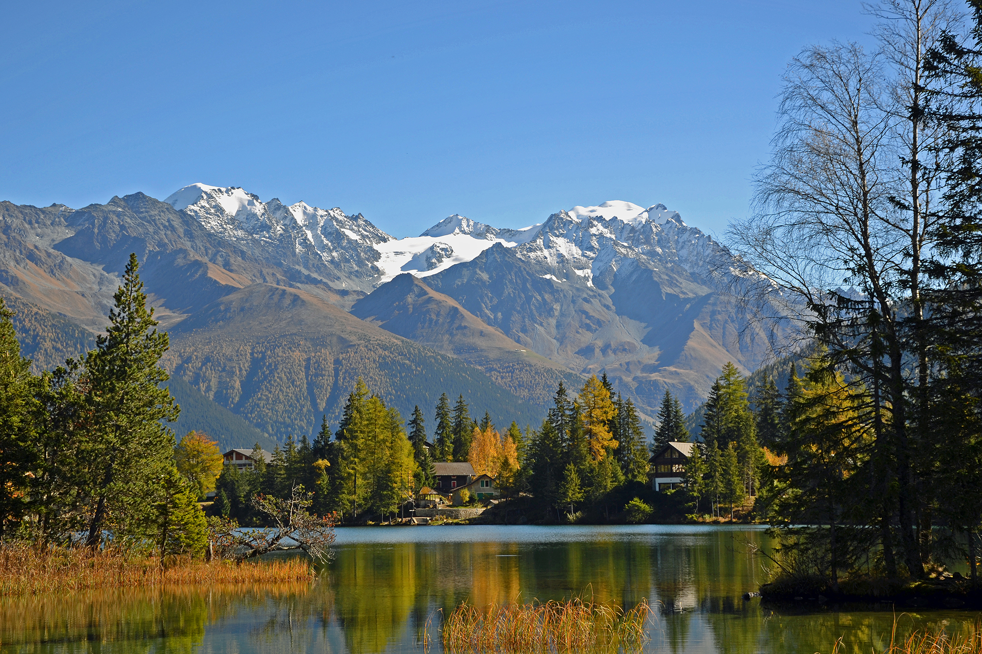 A picturesque scene in Champex-Lac Switzerland showcasing a charming challet nestled beneath a vast mountain. The calm waters of a serene lake reflect the cool winter landscape.