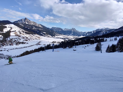 Winter scene at Schattwald-Zöblen in Tyrol, Austria showcasing a busy ski resort with a challet, set against a stunning backdrop of a majestic snow-covered mountain.