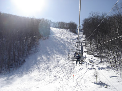 A winter scene at Catamount ski resort in Hudson Valley New York showcasing a ski lift transporting skiers up the snow-covered slopes with various winter sports being enjoyed around.