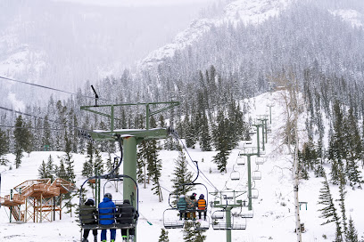 A winter sports scene at Sleeping Giant ski resort in Cody Wyoming. The snow-covered slopes of the mountain are dotted with skiers. A ski lift ascends the mountain ready for another round of excited skiers.