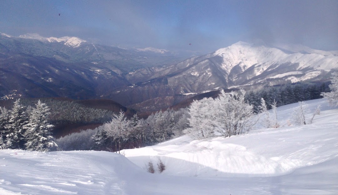 Breathtaking winter scenery at Doganaccia 2000 – Cutigliano in Tuscany, Italy, featuring a cozy chalet nestled against a snow-covered mountain, with traces of winter sports activities.
