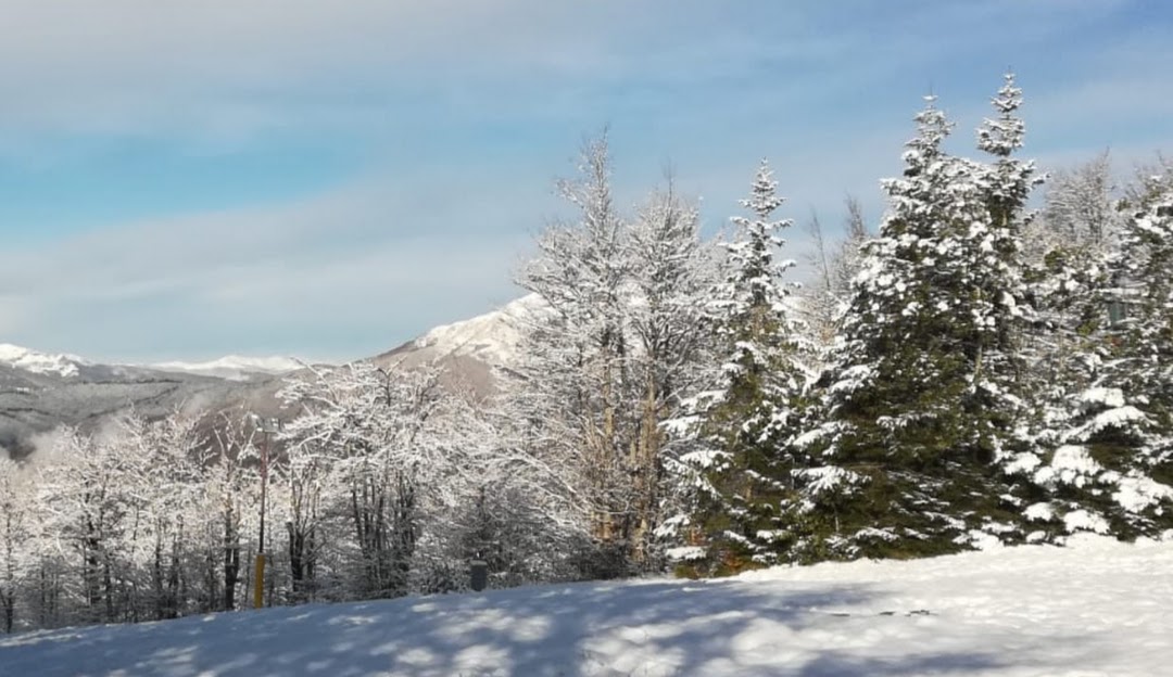 Winter scenery at Doganaccia 2000 – Cutigliano in Tuscany featuring snowy mountains, a bustling ski resort, and numerous winter sports activities in progress.