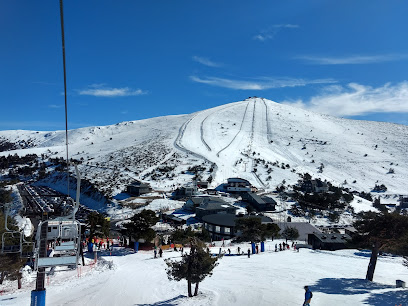 View of Puerto Navacerrada ski resort in Madrid, Spain showing slopes bustling with winter sports enthusiasts. A charming challet and a ski lift are nestled amid the mountain backdrop.
