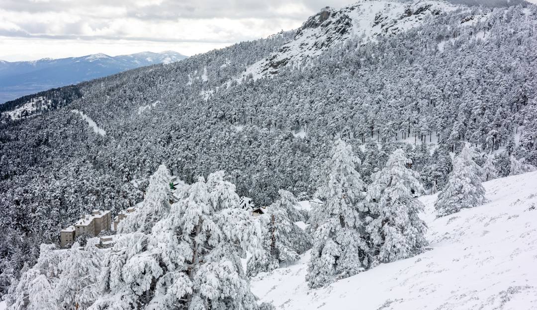 Winter sports enthusiasts enjoying a day at Puerto Navacerrada, Madrid, with a charming chalet seen nearby. The picturesque snowy mountain backdrop amplifies the beauty of the winter scene.