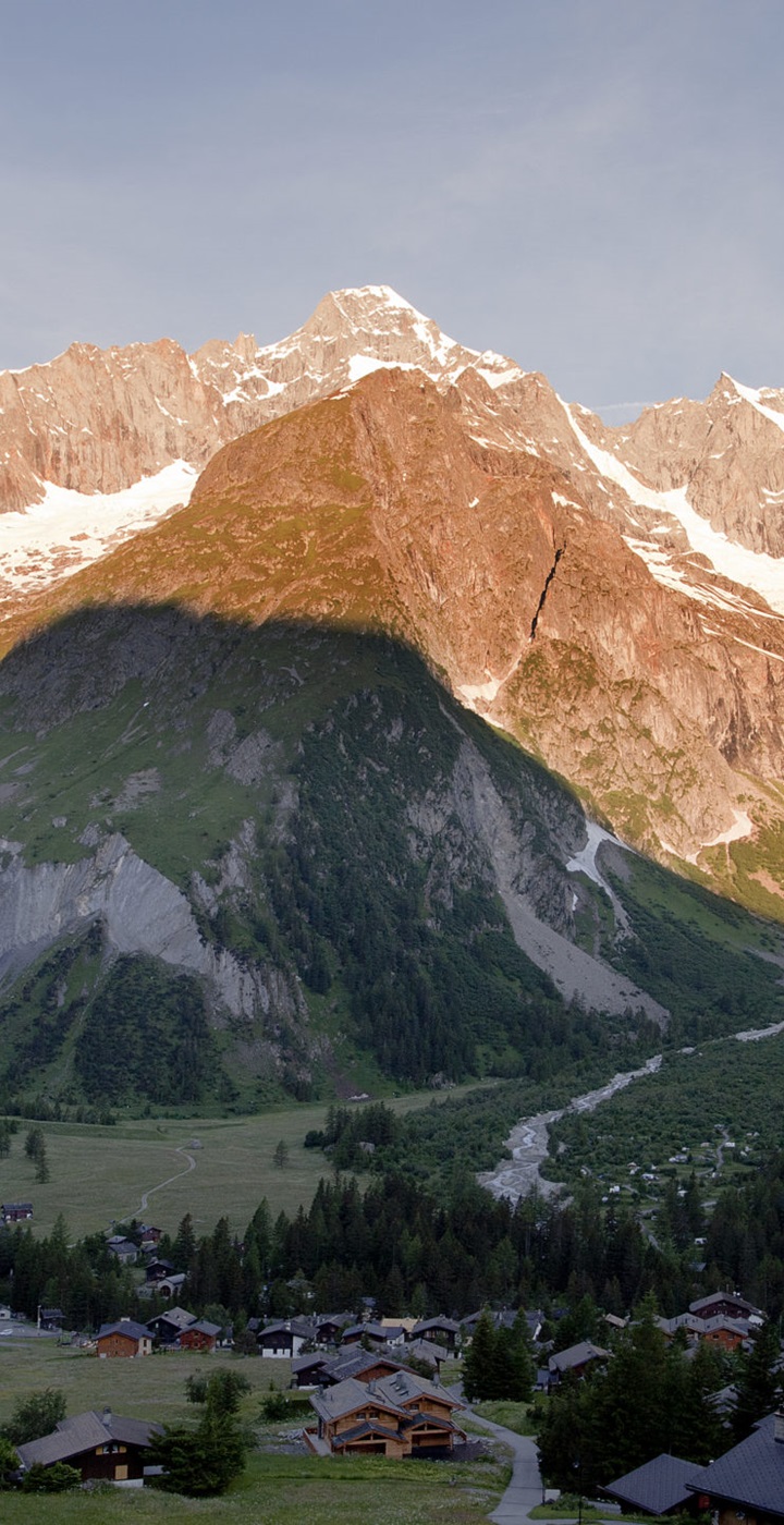 A striking image of the Swiss region La Fouly in Valais showcasing a majestic mountain in the backdrop. A charming chalet is nestled amid the scenery hinting at tranquillity and alpine beauty.