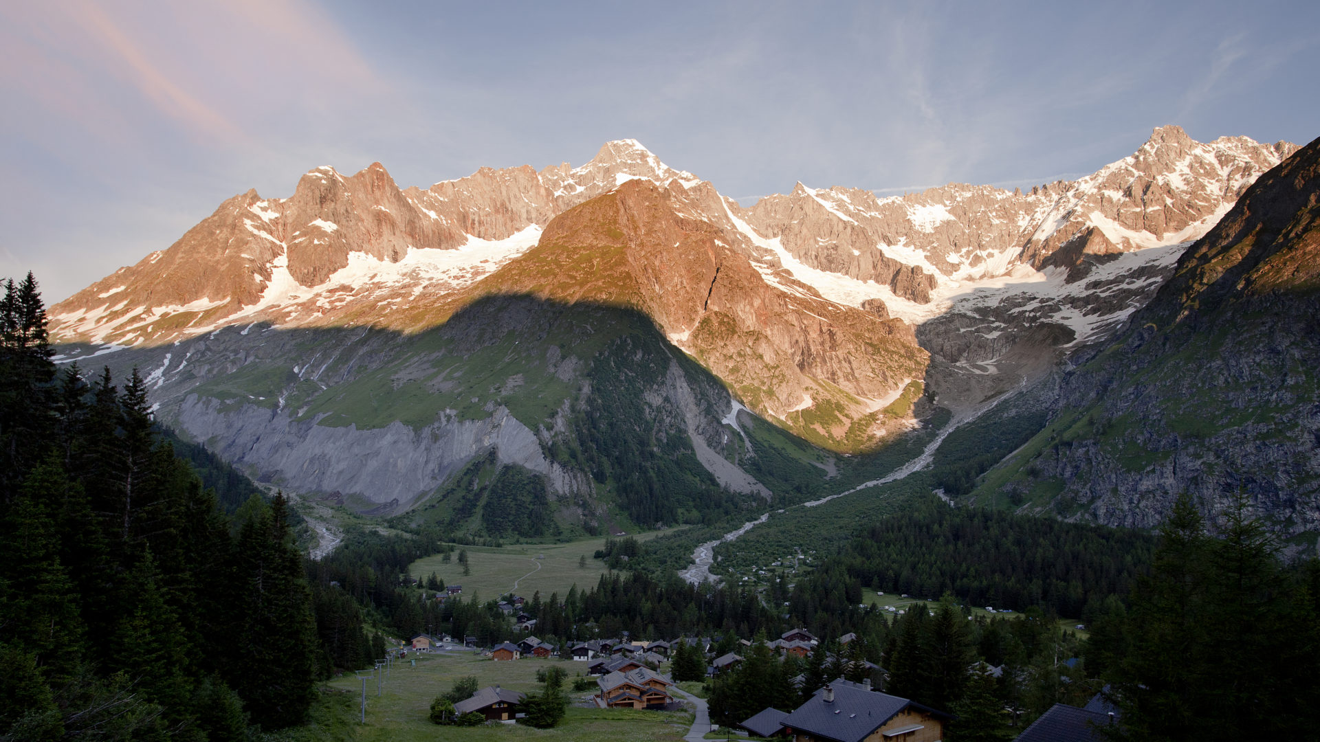 View of the serene La Fouly in Switzerland featuring a charming chalet nestled at the base of a towering snow-covered mountain. Part of a ski resort a mountain hut adds to the idyllic alpine scenery.