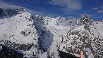 A magnificent mountain provides a picturesque backdrop to a challet nestled in the snowy La Fouly in Switzerland. Skiers navigates the slopes of the ski resort adding dynamic energy to the winter sports scene.