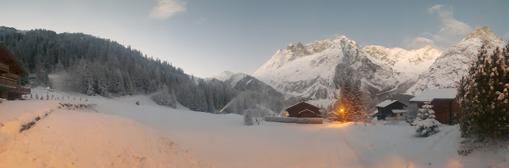 A winter sports scene in La Fouly Switzerland with a mountain hut in the foreground. Snow-covered slopes and a ski resort create a picturesque winter panorama.
