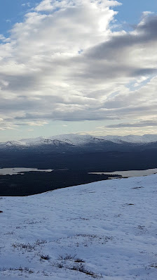 Winter scene at Trillevallen in Northern Sweden, featuring a dominant mountain set against a clear sky, a cosy chalet nestled at its base, and a skier gliding across fresh snow.
